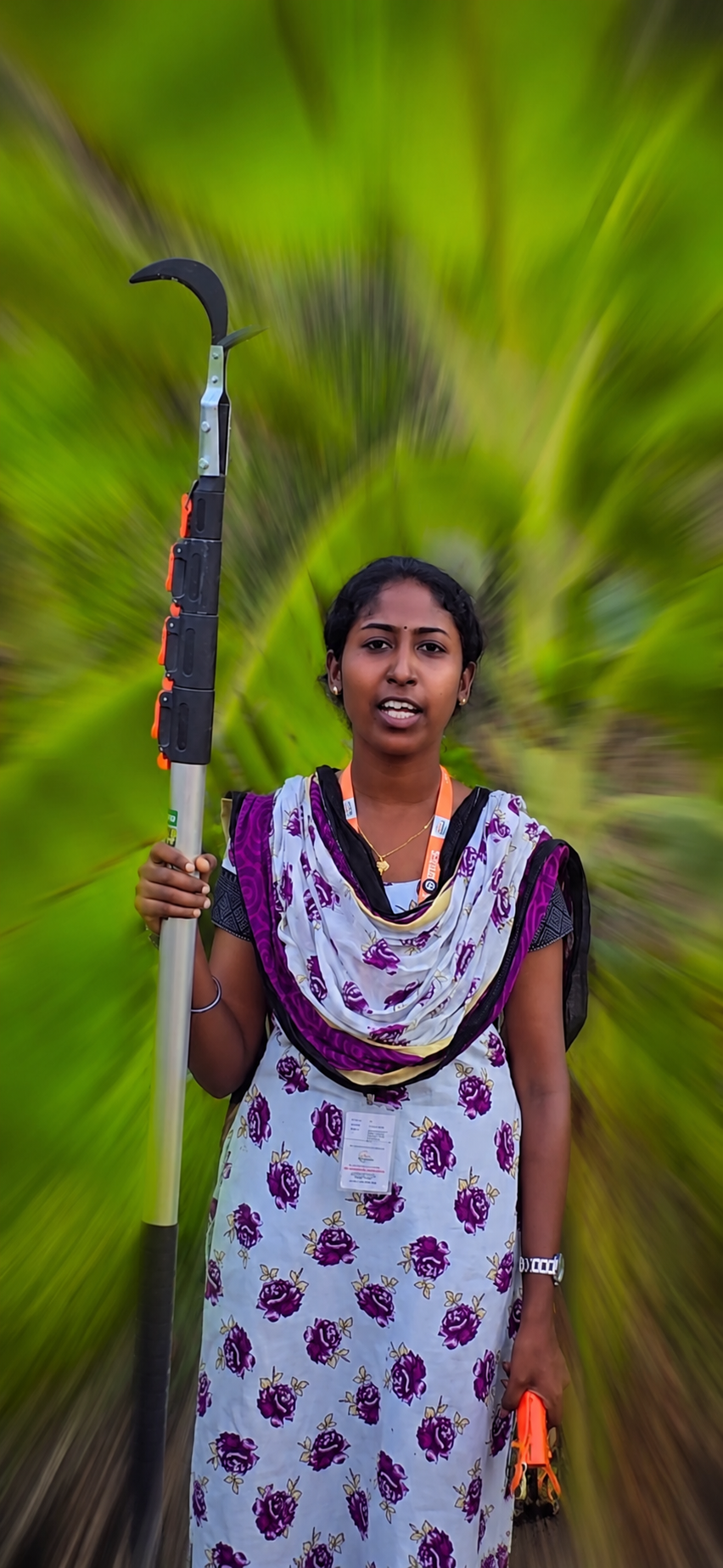A woman in a garden holding an extendable fruit plucker with a curved picking head